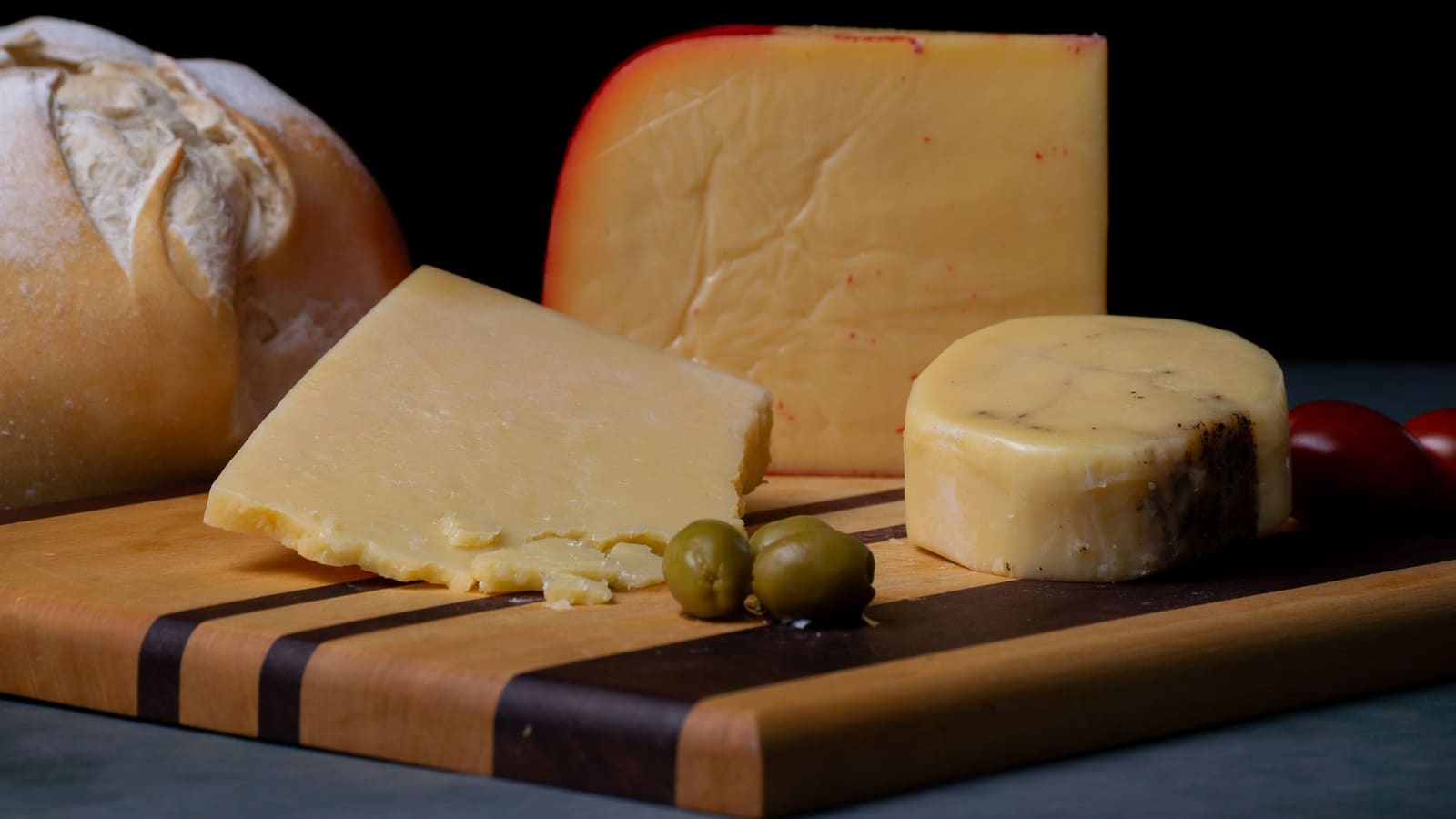 Wedges of hard cheese with a crusty loaf and olives on a wooden board