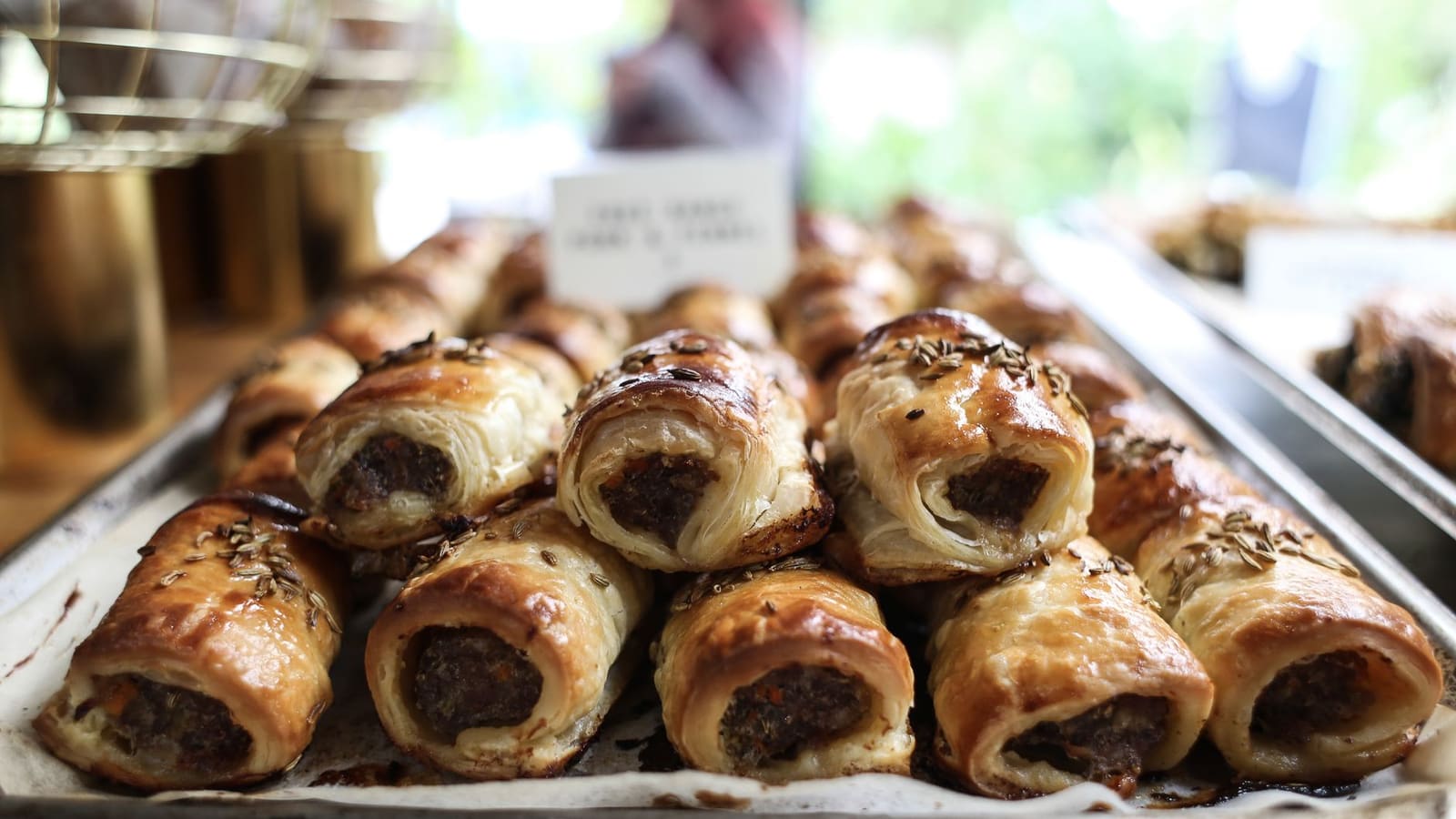 A tray of golden, flaky sausage rolls topped with fennel seeds