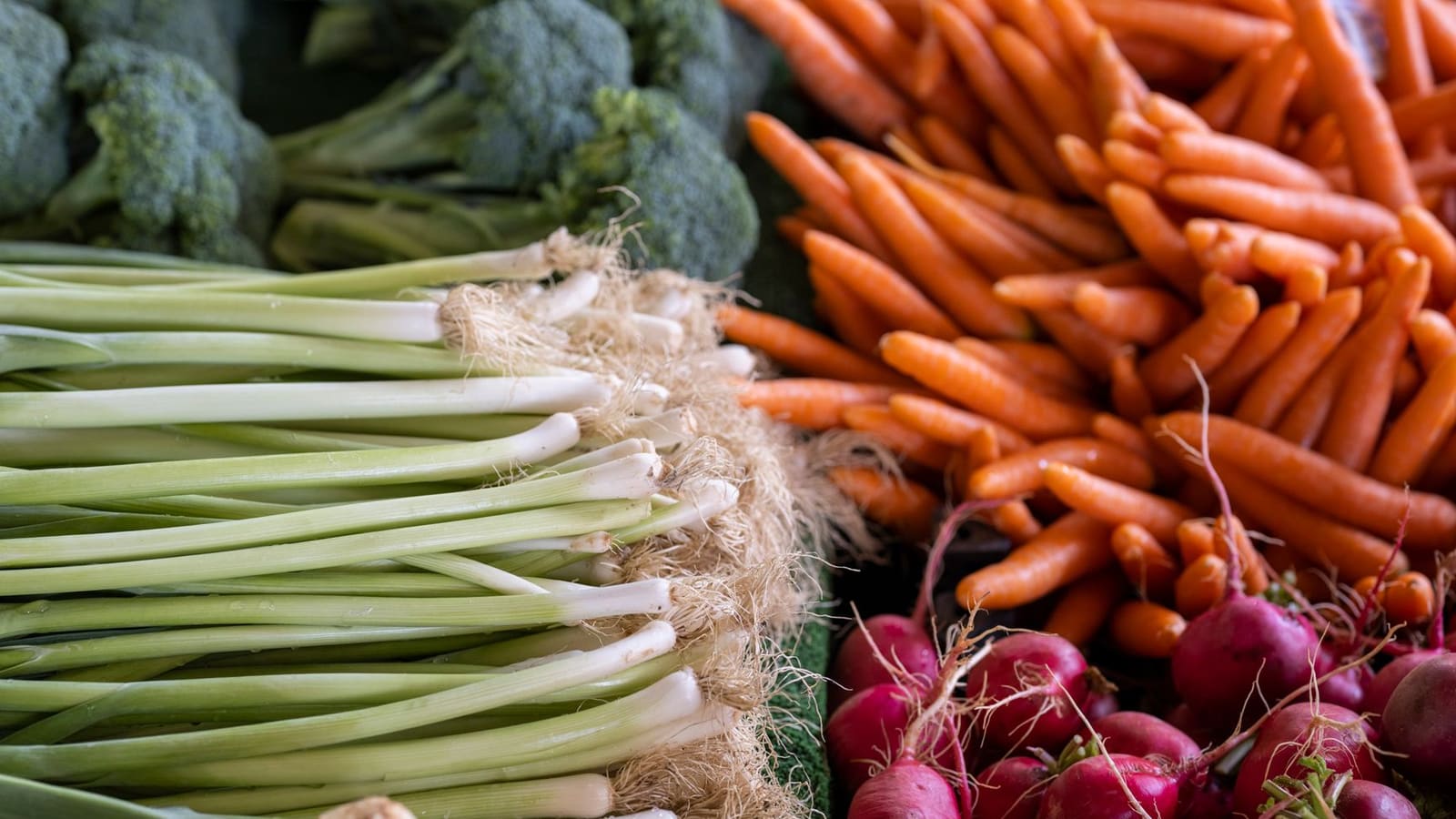 Fresh leeks, carrots, radishes and broccoli piled up on a market stall