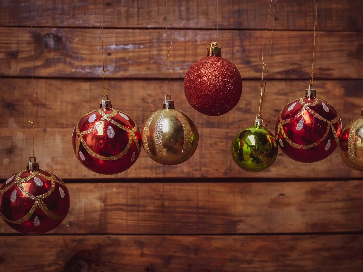 Red and gold glass Christmas baubles hanging against a wooden wall