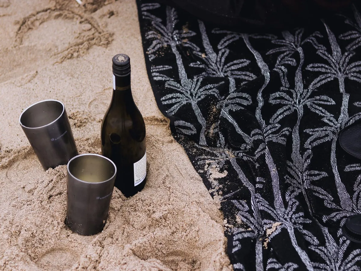 Two stainless steel cups and a bottle set in the sand on a beach