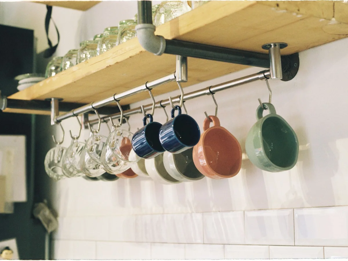 Colourful mugs hanging from hooks under a wooden kitchen shelf